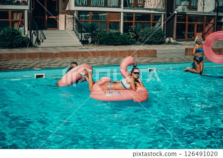 A woman is floating in a pink flamingo float in a pool. The pool is surrounded by a brick wall and has a few other people in the background. 126491020