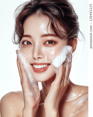 Smiling Korean woman applying foam cleanser to her face in a bright studio setting 126491225