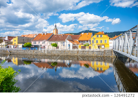 Sunlight reflects off the Otava River in Susice, Czechia, showcasing vibrant townhouses and a quaint bridge against a backdrop of blue skies and fluffy clouds. Sunlight reflects off the Otava River in Susice, Czechia, showcasing vibrant townhouses and a quaint bridge against a backdrop of blue skies and fluffy clouds. 126491272
