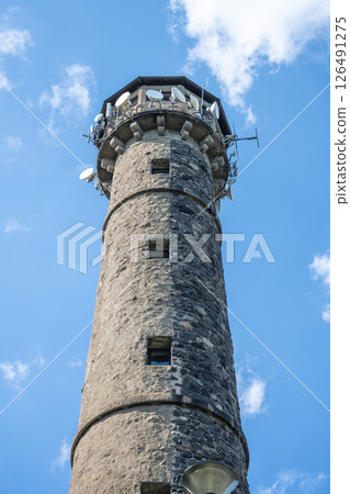 The Svatobor lookout tower rises prominently, crafted from stone, reaching towards a backdrop of clear blue sky. Surrounding greenery enhances its scenic beauty. 126491275