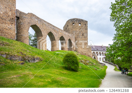 Visitors explore the Gothic Bridge of Velhartice Castle in Czechia, surrounded by lush greenery and historical stone architecture, linking the castle's structures. An atmospheric experience awaits. 126491288