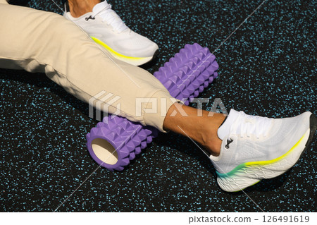 Athlete man stretching legs and check trigger point on foam roller on sports ground. Outdoors. Myofascial Release. 126491619