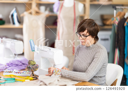 Female clothing designer stitching fabric on sewing machine in studio Female clothing designer stitching fabric on sewing machine in studio 126491920
