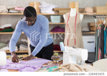 Experienced dressmaker drawing chalk lines on linen fabric in studio Experienced dressmaker drawing chalk lines on linen fabric in studio 126491935