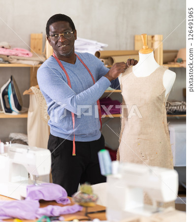Male tailor sews new dress on a mannequin in sewing studio 126491965