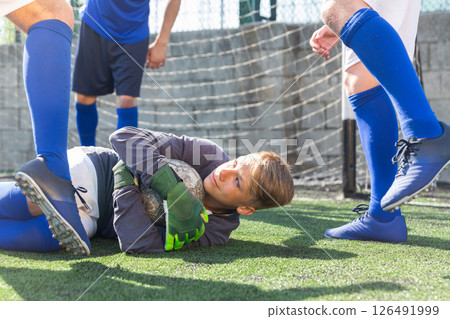 Goalkeeper with ball lies on grass in penalty area. Young teen soccer game 126491999