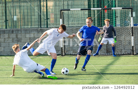 Game of football match between two teams of teenagers in white and blue shirts Game of football match between two teams of teenagers in white and blue shirts 126492012