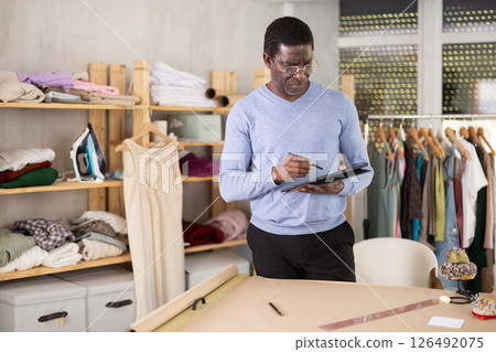 African American man tailor creates sketch of dress on tablet 126492075