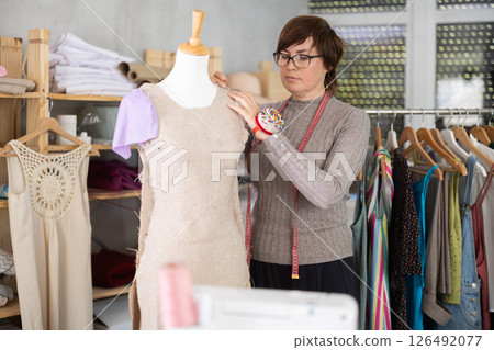 Woman tailor connects parts of dress on mannequin. Woman tailor connects parts of dress on mannequin. 126492077