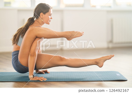 Female coach practicing bakasana yoga pose on mat in fitness studio Female coach practicing bakasana yoga pose on mat in fitness studio 126492167