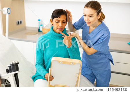 Beautician examining face skin of female patient Beautician examining face skin of female patient 126492188