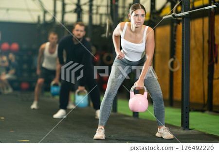 Fit girl doing exercises with kettlebell during group workout 126492220