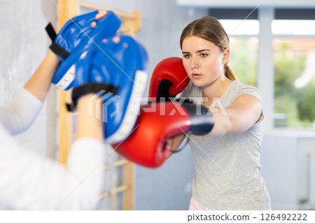 Girls works out strength and speed of boxing punch mitts with help of partner in boxing paws 126492222