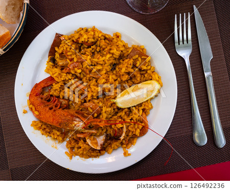 Paella made of rice and different seafood served in plate with table appointments 126492236