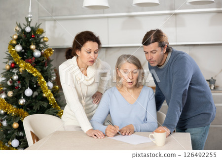 Married couple helps elderly mother write testament in kitchen at christmas Married couple helps elderly mother write testament in kitchen at christmas 126492255