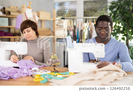 Working in sewing workshop - man and woman working at sewing machines, creating new clothes 126492258