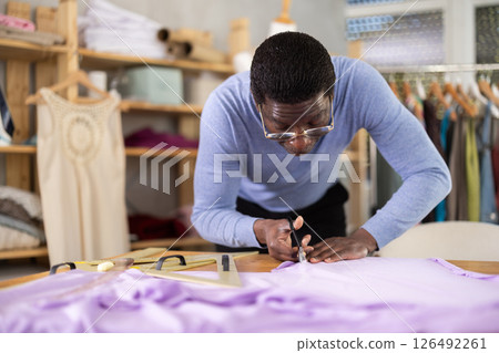 Male dressmaker cutting lavender fabric in sewing workshop 126492261