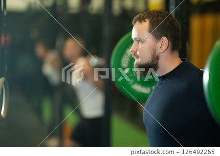 Determined young guy working out with weight rod during crossfit workout 126492265