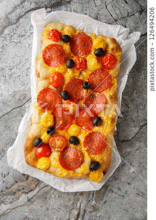 Homemade Italian pinsa with cherry tomatoes, peperoni sausage, olive and cheddar cheese closeup on parchment paper. Vertical top view Homemade Italian pinsa with cherry tomatoes, peperoni sausage, olive and cheddar cheese closeup on parchment paper. Vertical top view 126494206