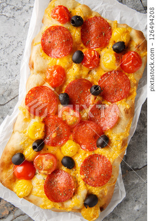 Pinsa Romana with cherry tomatoes, peperoni sausage, olive cheddar cheese closeup on parchment paper. Vertical top view Pinsa Romana with cherry tomatoes, peperoni sausage, olive cheddar cheese closeup on parchment paper. Vertical top view 126494208