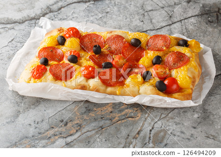 Fragrant homemade pinsa romana with tomato mix, peperoni sausage, black olive and cheddar cheese closeup on parchment paper. Horizontal 126494209