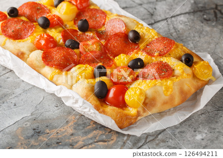 Italian pinsa romana with tomato mix, peperoni sausage, olive and cheddar cheese closeup on parchment. Horizontal 126494211