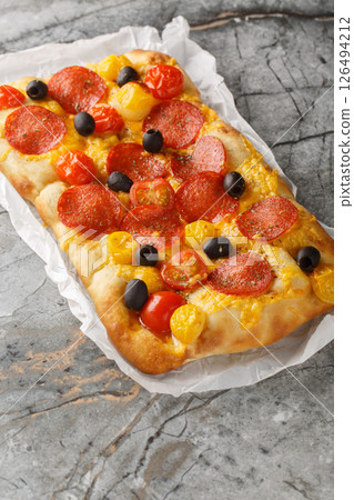 Homemade Italian pinsa with cherry tomatoes, peperoni sausage, olive and cheddar cheese closeup on parchment paper. Vertical 126494212