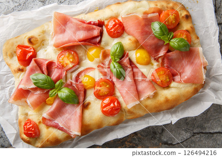 Italian pinsa romana with tomato mix, prosciutto, mozzarella cheese and basil on parchment paper. horizontal top view 126494216