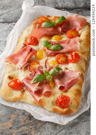Pinsa Romana with with cherry tomatoes, ham, mozzarella cheese and basil closeup on parchment paper. Vertical Pinsa Romana with with cherry tomatoes, ham, mozzarella cheese and basil closeup on parchment paper. Vertical 126494224