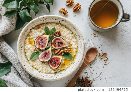 Healthy breakfast bowl with oatmeal, figs, nuts, and herbal tea on a rustic table setting Healthy breakfast bowl with oatmeal, figs, nuts, and herbal tea on a rustic table setting 126494715