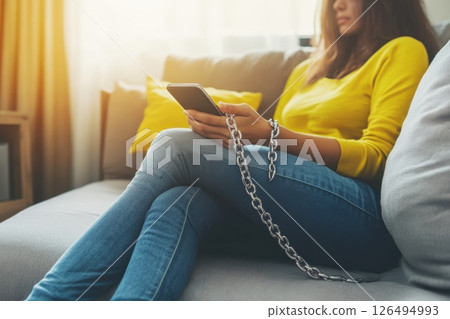 Woman in Yellow Sweater Using Smartphone While Chained to Sofa in Cozy Living Room Woman in Yellow Sweater Using Smartphone While Chained to Sofa in Cozy Living Room 126494993