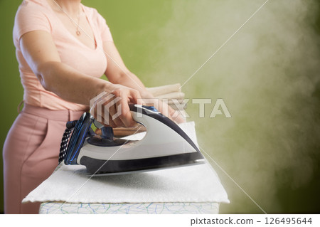 Steaming iron on clothes with olive green wall Steaming iron on clothes with olive green wall 126495644