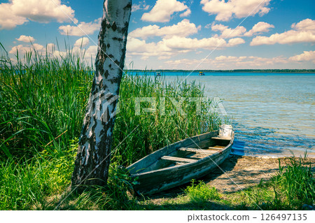 View of the lake in summer on a sunny day. Wooden boat on the lakeshore 126497135
