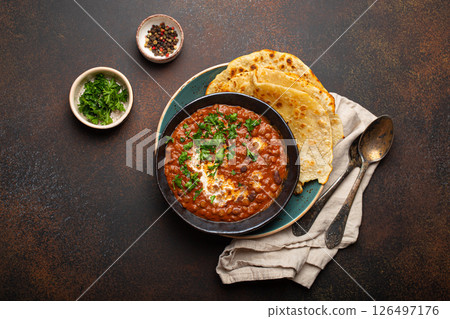 Traditional Indian Punjabi dish Dal makhani with lentils and beans in black bowl served with naan flat bread, fresh cilantro and two spoons on brown concrete rustic table top view Traditional Indian Punjabi dish Dal makhani with lentils and beans in black bowl served with naan flat bread, fresh cilantro and two spoons on brown concrete rustic table top view 126497176