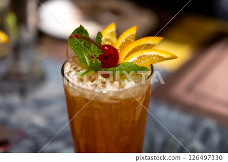 Close up view of orange cocktail, with cherry and sliced orange on top. On the table with bokeh background 126497330