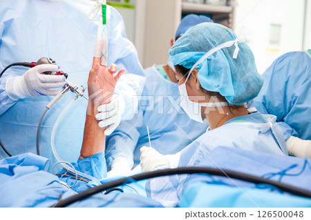 Group of orthopedic surgeons performing a wrist arthroscopy on a male patient. Female doctor performing a surgery. Orthopedic surgeon. Surgery and insurance concept. 126500048