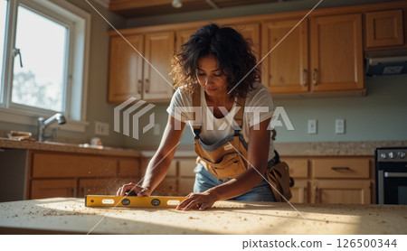 Female furniture installer using level tool in kitchen renovation 126500344