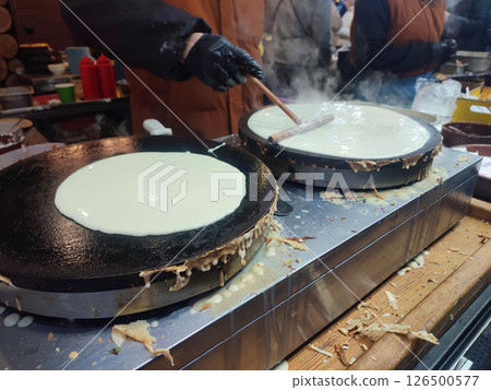 Frying pancakes. Person chef spreading liquid batter on round frying pan spatula. Cooking food on street. Festivities festival. Street food fried batter dough. Vertical 126500577