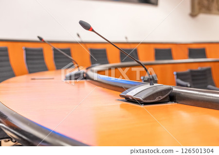 Microphones and round brown table in an empty conference room. Beginning of session meeting with black chair 126501304