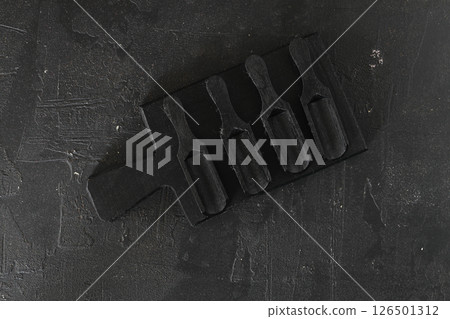 Black burnt wooden empty kitchenware cutting board, plates, scoop and spoon over black wood background Black burnt wooden empty kitchenware cutting board, plates, scoop and spoon over black wood background 126501312