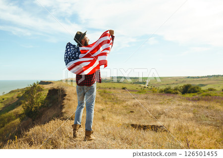 4th of July. American Flag. Traveler with the flag of America. The man in a hat, a backpack, a shirt and jeans. 4th of July. American Flag. Traveler with the flag of America. The man in a hat, a backpack, a shirt and jeans. 126501455
