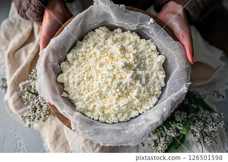 Homemade fresh cheese in a wooden bowl held by hands, surrounded by delicate flowers in soft lighting Homemade fresh cheese in a wooden bowl held by hands, surrounded by delicate flowers in soft lighting 126501598