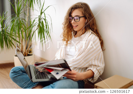 Cute woman using laptop while sitting on floor at home. Remote work from home. Freelancing concept. Cute woman using laptop while sitting on floor at home. Remote work from home. Freelancing concept. 126501617