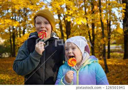 Portrait of a boy and a girl eating lollipops in an autumn park. Portrait of a boy and a girl eating lollipops in an autumn park. 126501941