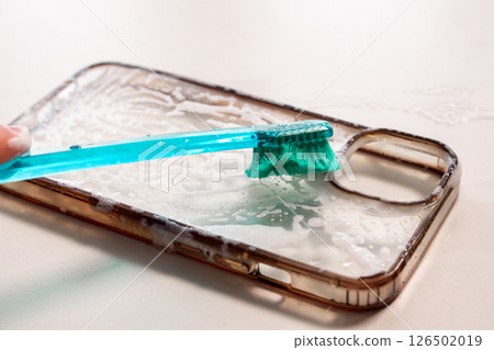 Transparent phone case being cleaned with toothbrush and soap, showcasing before and after use, highlighting the difference in clarity and cleanliness for effective visual storytelling Transparent phone case being cleaned with toothbrush and soap, showcasing before and after use, highlighting the difference in clarity and cleanliness for effective visual storytelling 126502019
