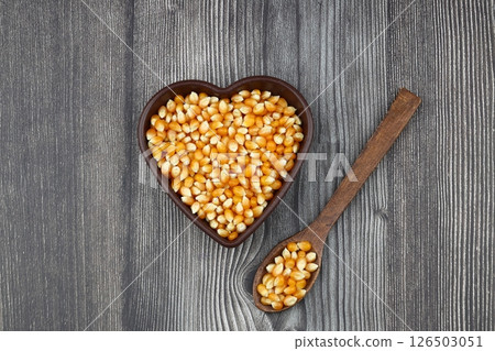 Unpopped popcorn in a wooden bowl on wooden background. A type of corn that expands from the kernel and puffs up when heated. Yellow seeds, edible, raw and vegan food. Isolated macro photo close up. 126503051