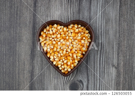 Unpopped popcorn in a wooden bowl on wooden background. A type of corn that expands from the kernel and puffs up when heated. Yellow seeds, edible, raw and vegan food. Isolated macro photo close up. 126503055