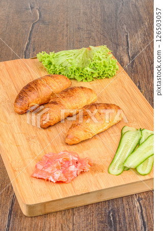 Croissants and ingredients for filling with lettuce leaves, pieces of red fish and cucumbers. Croissants and ingredients for filling with lettuce leaves, pieces of red fish and cucumbers. 126503057