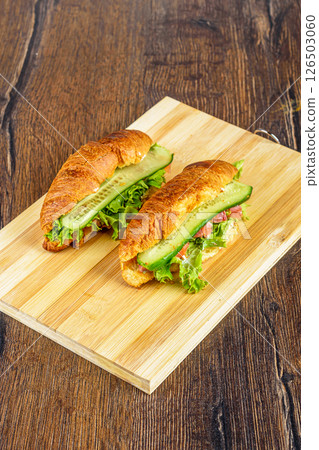 Cutting board with croissants stuffed with lettuce leaves and soft cheese, pieces of red fish and cucumbers. 126503060
