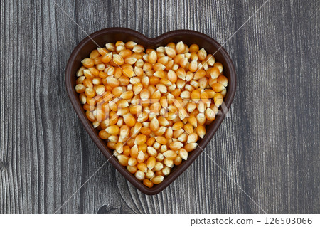 Unpopped popcorn in a wooden bowl on wooden background. A type of corn that expands from the kernel and puffs up when heated. Yellow seeds, edible, raw and vegan food. Isolated macro photo close up. 126503066